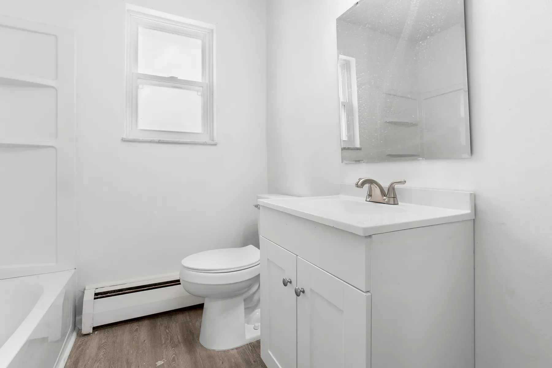 Renovated bathroom with a white vanity and framed mirror