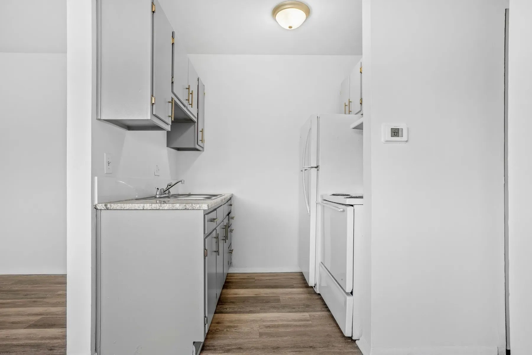 Galley kitchen with white appliances and wood-look flooring